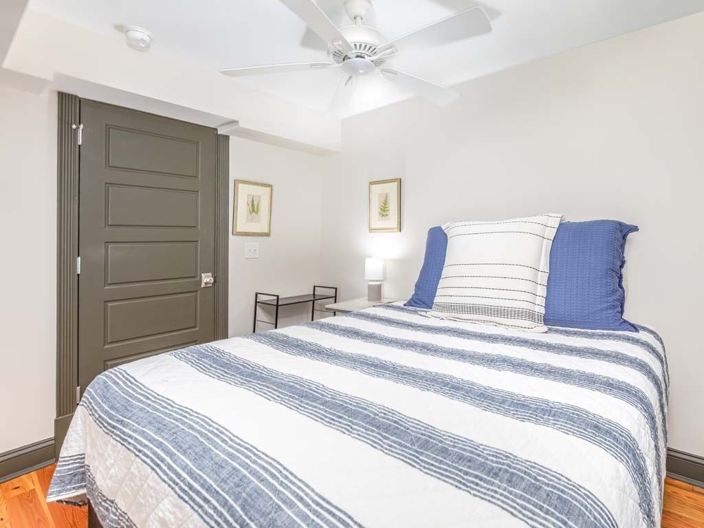 A bedroom with a bed, a ceiling fan, a door, and framed pictures on the wall.
