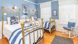 Une chambre avec deux lits, un fauteuil à bascule et un ventilateur de plafond.