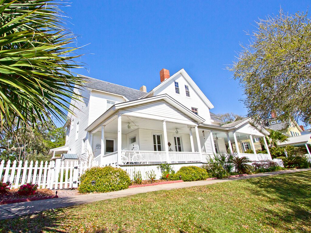 A two-story white house with a front porch, a picket fence, and well-maintained landscaping.