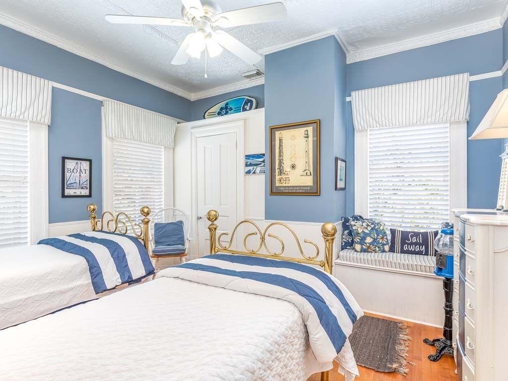 A bedroom with two beds, a ceiling fan, a radiator, and a framed picture on the wall.