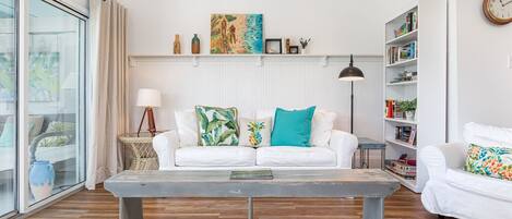 A modern living room with a white sofa, a coffee table, and a bookshelf.