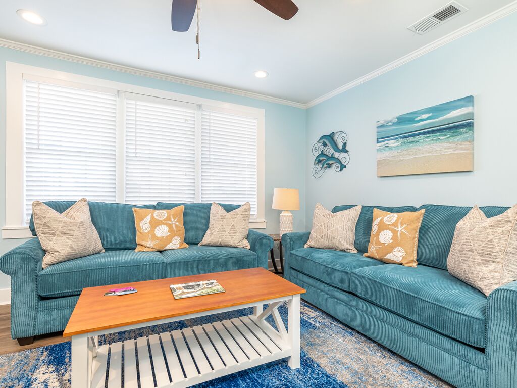 A living room with two teal sofas, a wooden coffee table, and a blue patterned rug.