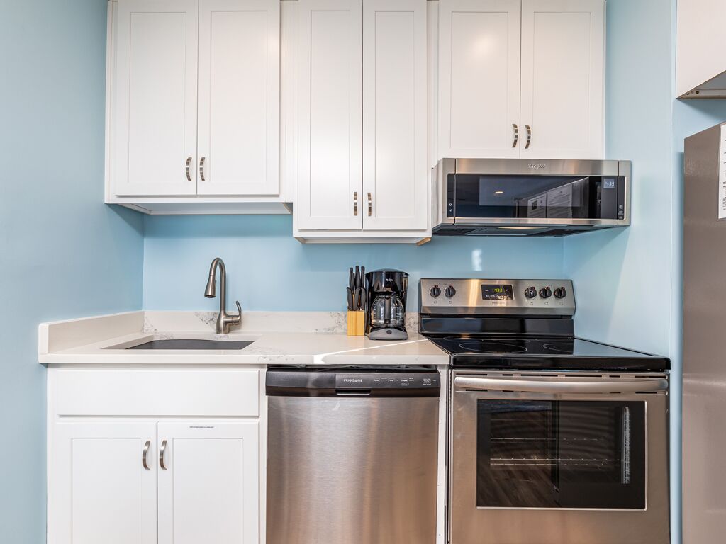 A modern kitchen with white cabinets, a stainless steel dishwasher, a black stove, and a microwave.