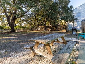 Ein Holztisch für ein Picknick in einem Garten mit einem großen Baum und einem Haus im Hintergrund.