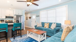 A modern living room with a teal sofa set, a wooden coffee table, and a ceiling fan. - Walkin On Sunshine by Tybee Vacation Rentals (Tybee Island)
