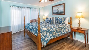 A bedroom with a wooden four-poster bed, a ceiling fan, a nightstand with a lamp, and a framed picture on the wall. - Walkin On Sunshine by Tybee Vacation Rentals (Tybee Island)