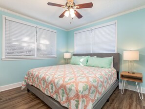 Ein Schlafzimmer mit einem Bett, zwei Nachttischlampen, einem Deckenventilator und zwei Fenstern mit Jalousien.