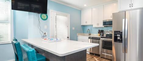A modern kitchen with white cabinets, a stainless steel refrigerator, and a central island with teal chairs.