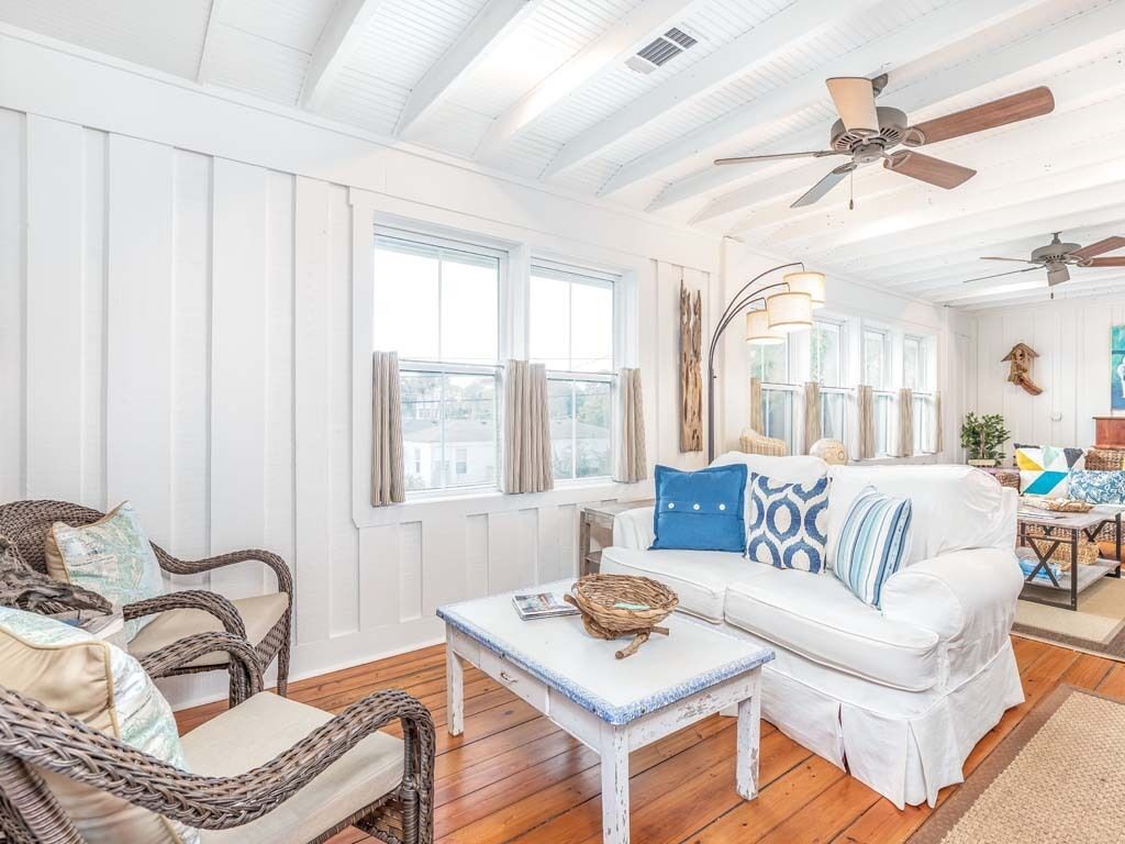 A bright, airy living room with a white sofa, wicker chairs, and a ceiling fan.