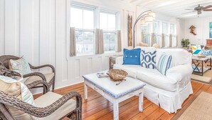 A bright, airy living room with a white sofa, wicker chairs, and a ceiling fan. - Wrens Nest by Tybee Vacation Rentals (Tybee Island)