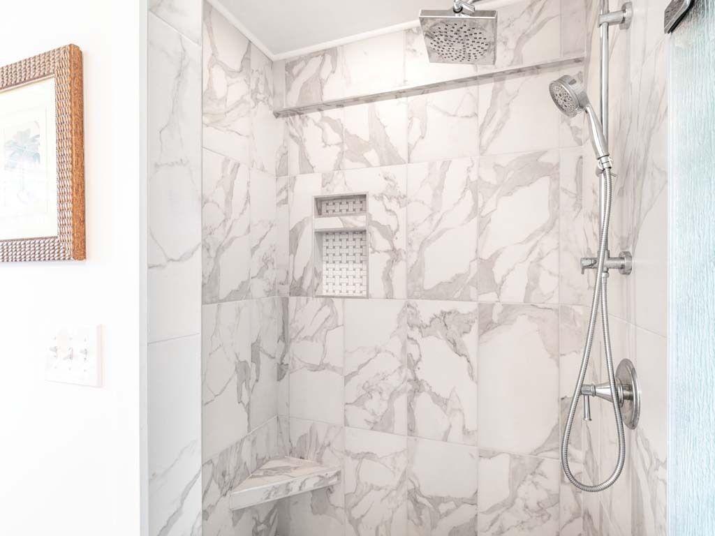 A bathroom with marble walls, a shower, and a small shelf.