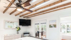 A bedroom with a bed, a ceiling fan, a TV, a dresser, and a window with a view. - Wrens Nest by Tybee Vacation Rentals (Tybee Island)
