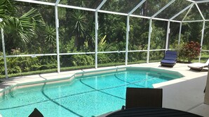 Zona de piscina con cerramiento de vidrio, sillas de descanso y una mesa.