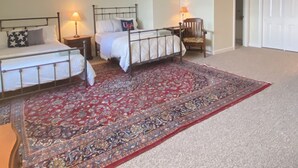 A bedroom with two beds, a red patterned rug, and a white door.