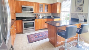 A kitchen with wooden cabinets, a microwave, an oven, a sink, and a bar area with two stools.
