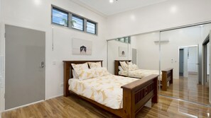A bedroom with a wooden bed, a large mirror, and a door. - Searenity on Castle hill (Castle Hill)
