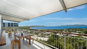 A balcony with a wooden table and chairs, overlooking a coastal area with houses and a clear blue sky. - Searenity on Castle hill (Castle Hill)