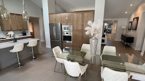 A modern kitchen with a glass dining table, white chairs, stainless steel appliances, and wooden cabinets. - Luxurious modern 3-bedroom plus den home w/ pool & hot tub (Phoenix)