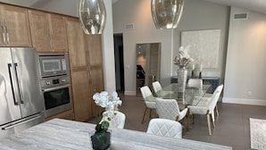 A modern kitchen with stainless steel appliances, a marble countertop, and a dining area with a glass table and white chairs. - Luxurious modern 3-bedroom plus den home w/ pool & hot tub (Phoenix)