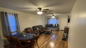 A living room with a dining table, chairs, a sofa, and two ceiling fans.