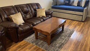 A living room with a brown leather sofa, a wooden coffee table, and a blue sofa with patterned cushions.