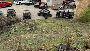 A gravel parking area with various off-road vehicles and a small building with a porch.