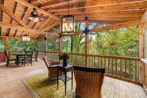 Una terraza de madera con una mesa y sillas, rodeada de grandes ventanales que dan a un bosque.