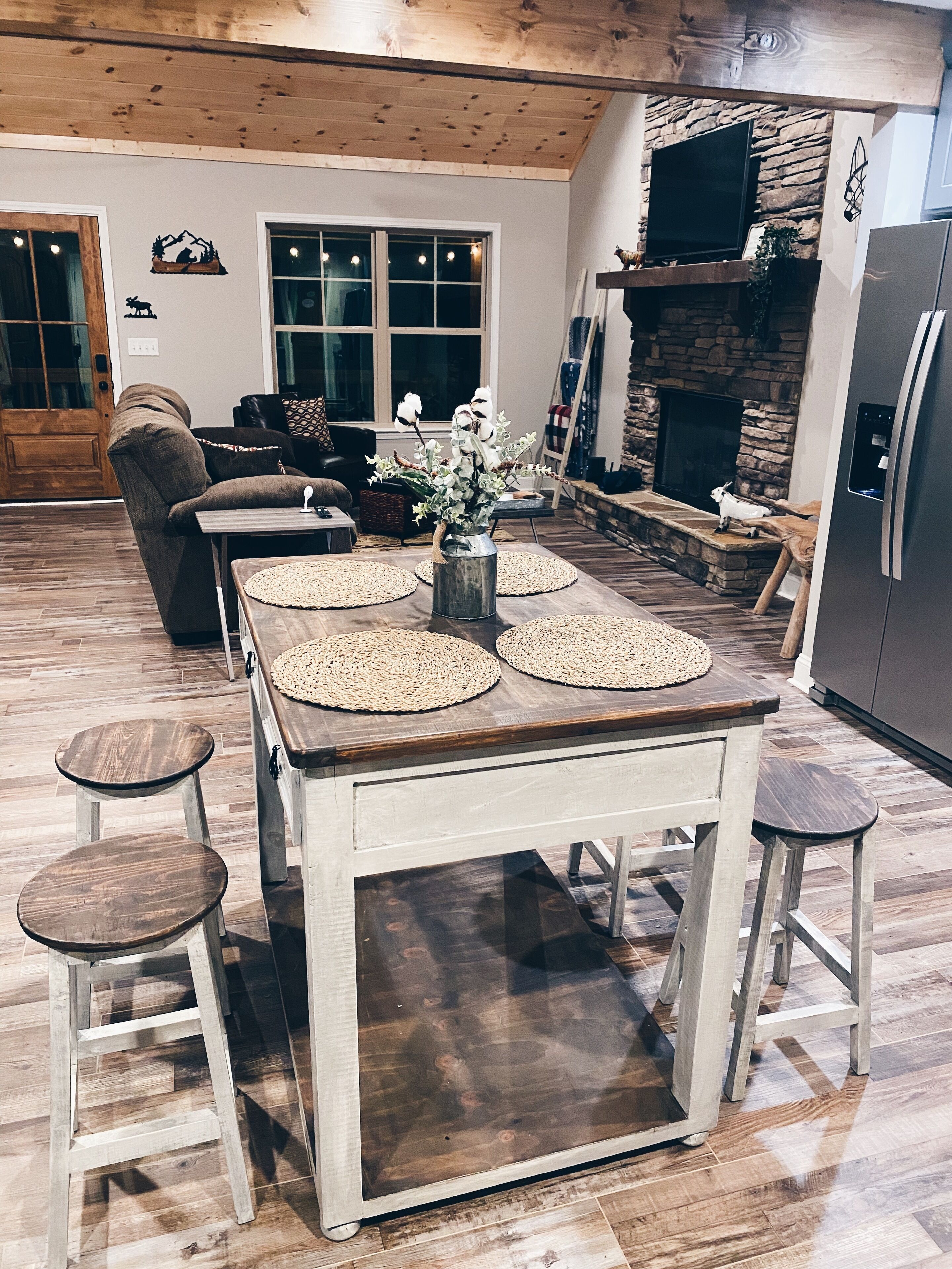 Un comedor con una mesa de madera, cuatro taburetes y un jarrón de flores.