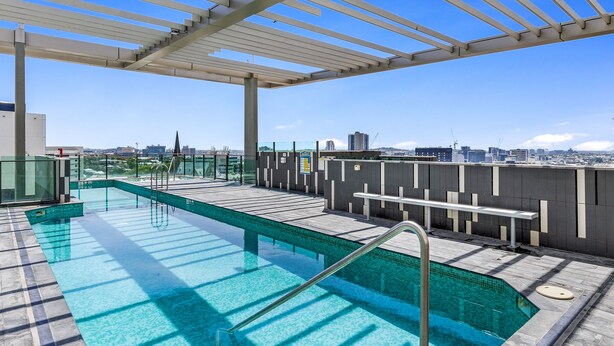 A rooftop swimming pool with clear blue water, a pergola, and a city view. - Quattro Apartments (Spring Hill)