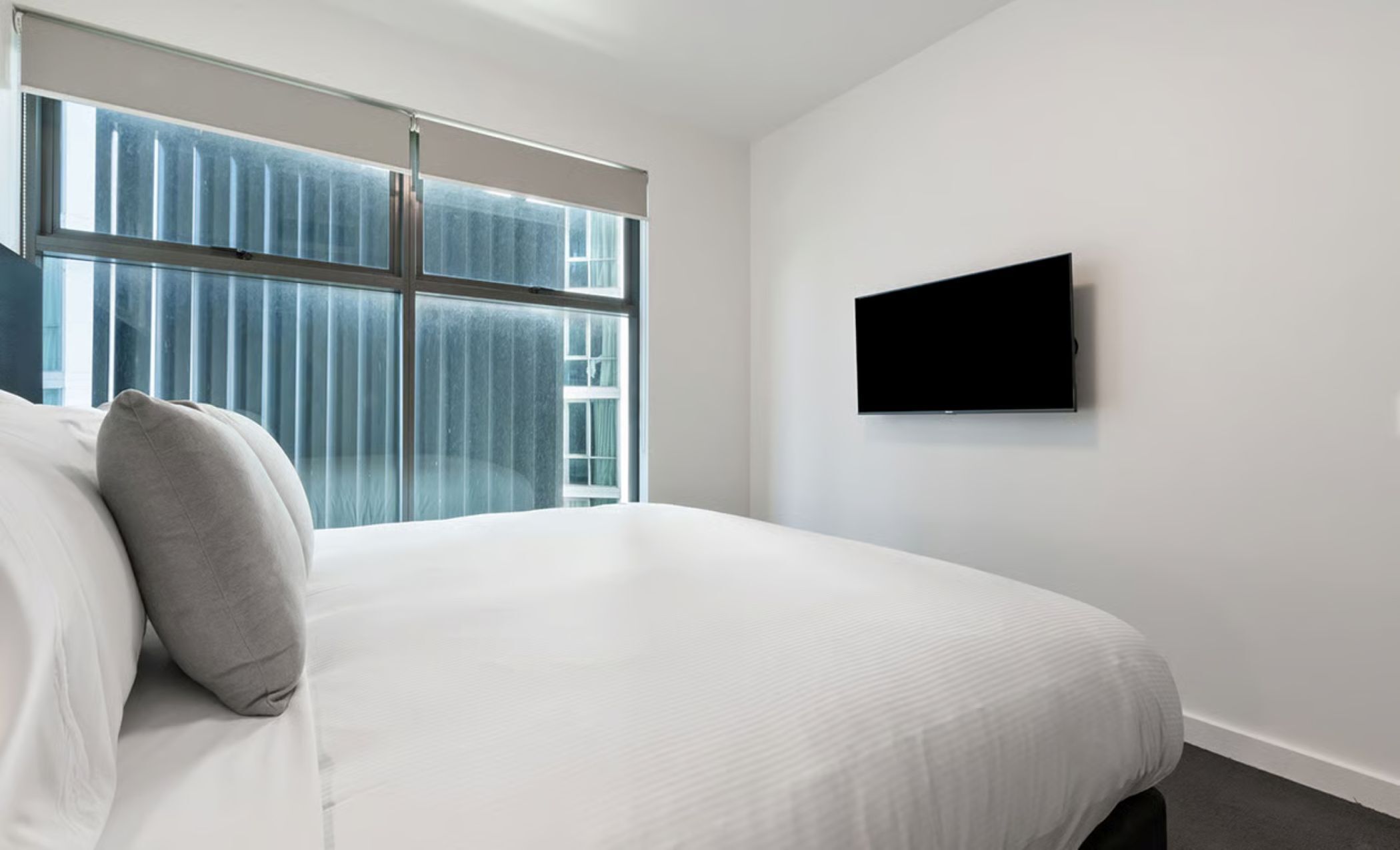 Habitación de hotel con una cama grande, un televisor de pantalla plana en la pared y una ventana con persianas.