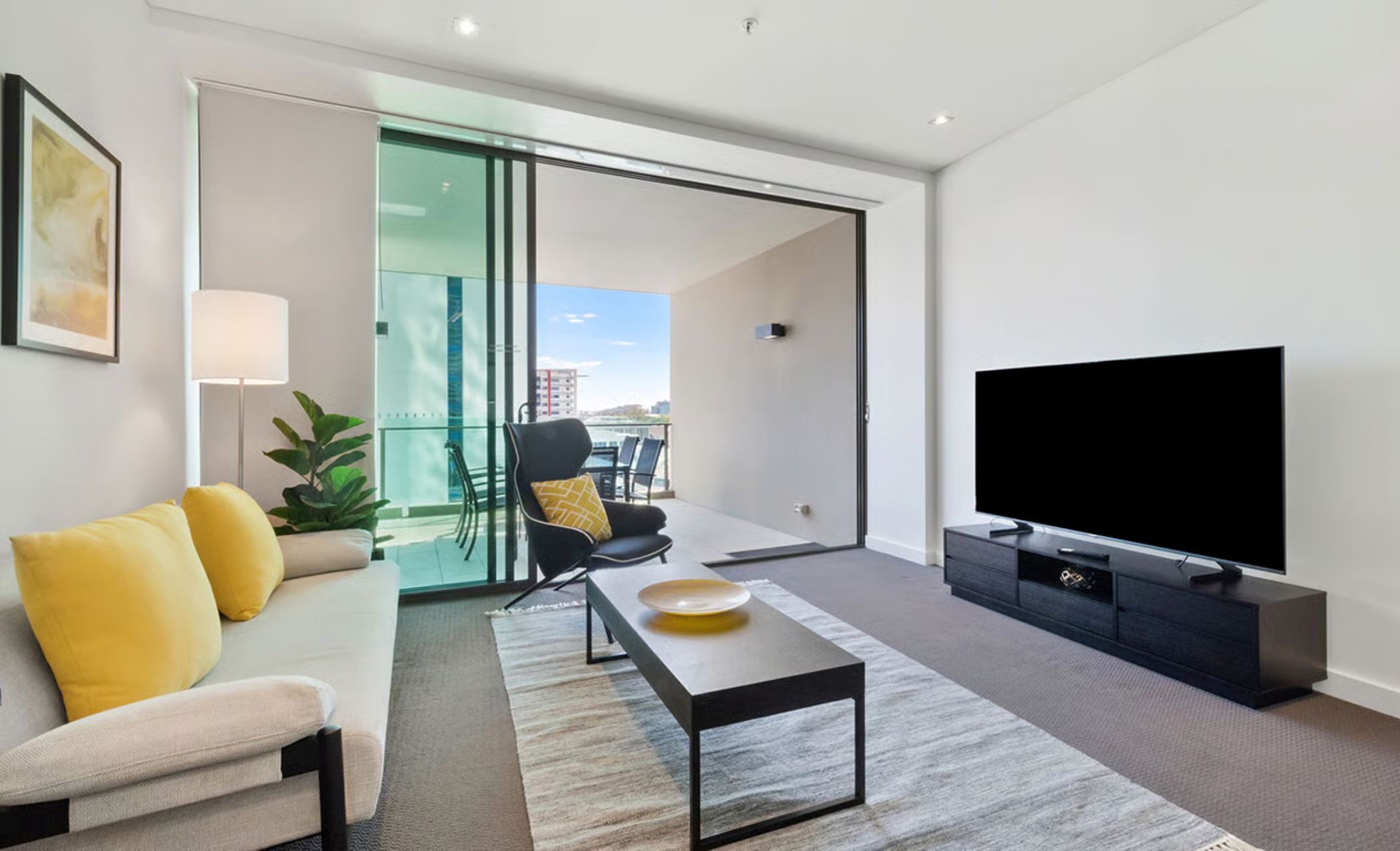A modern living room with a sofa, a coffee table, a TV, and a sliding glass door leading to an outdoor area.