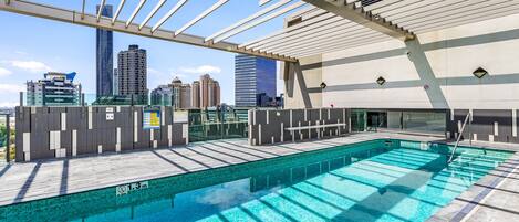 Una piscina en la azotea con vistas al horizonte de la ciudad, un área techada con asientos y un letrero que indica 'no saltos'.