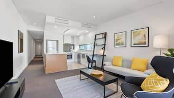 Una sala moderna con sofá, mesa de centro y televisor. Se aprecia una cocina al fondo con zona de comedor.