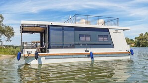 Ein modernes Hausboot mit einer überdachten Deckfläche, einem kleinen Fenster und dem Namen "mini INDEPENDENT" an der Seite.