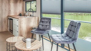 Eine kompakte Küche mit Spüle, Herd und Fenster mit Blick auf ein Gewässer. Zwei Stühle und ein kleiner Tisch mit Kerzenhalter sind vorhanden.