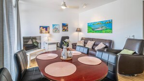 A modern living room with a brown leather sofa, a dining table with placemats, a TV, and artwork on the walls. - Amazing apartment in Málaga with WiFi (Málaga)