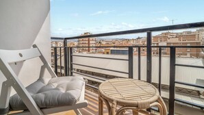 A balcony with a white chair and a wicker table, overlooking a cityscape with buildings and a clear sky. - Amazing apartment in Málaga with WiFi (Málaga)