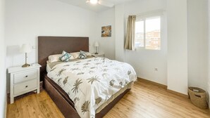 A bedroom with a bed, nightstands, a ceiling fan, a window with curtains, and a view of buildings outside. - Amazing apartment in Málaga with WiFi (Málaga)