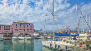 Ein Yachthafen mit mehreren vertäuten Booten, ein Gebäude mit rosafarbenem Mauerwerk und einem strahlend blauen Himmel.