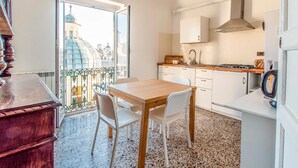 Eine kleine Küche mit Essbereich, Blick auf ein Gebäude durch eine Glastür und ein Balkon mit Geländer.