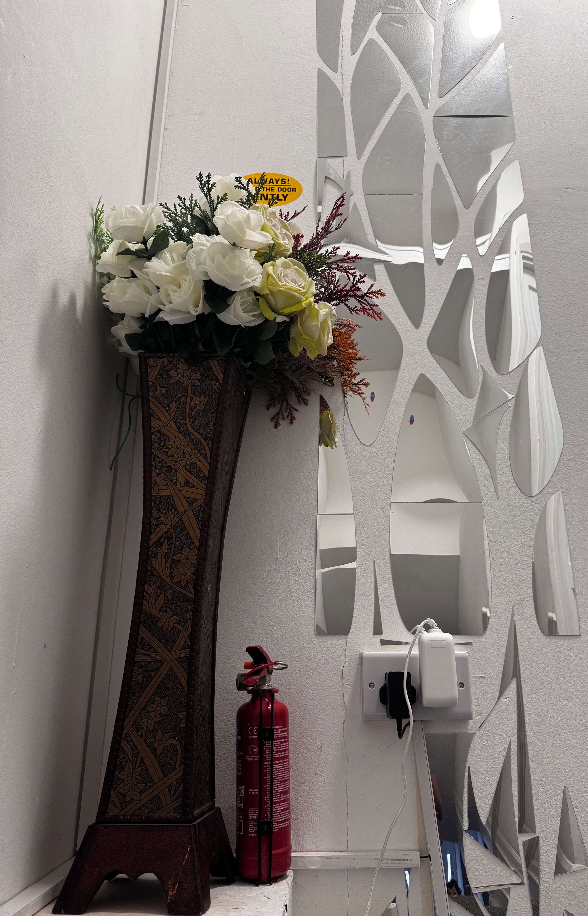 A decorative vase with flowers on a wall, a fire extinguisher, and a power outlet.