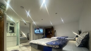 A modern bedroom with a large bed, a TV mounted on the wall, and a bathroom visible through an open door. - Heathrow Garden Lodge [Free Parking • Netflix • Prime • Coffee • WiFi] (Hayes)