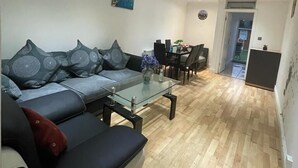 A modern living room with a sofa, a glass coffee table, and a dining area with chairs and a table. - Heathrow Garden Lodge [Free Parking • Netflix • Prime • Coffee • WiFi] (Hayes)