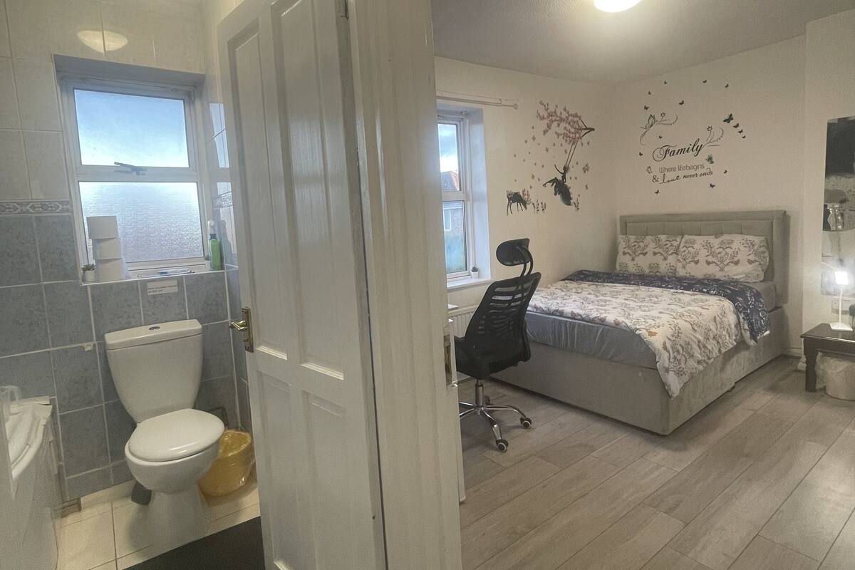 Een slaapkamer met een bed, een stoel, een bureau en een badkamer met toilet en wastafel.