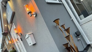A building exterior with multiple wall-mounted light fixtures, a mailbox, and a planter with tall plants. - Heathrow Garden Lodge [Free Parking • Netflix • Prime • Coffee • WiFi] (Hayes)