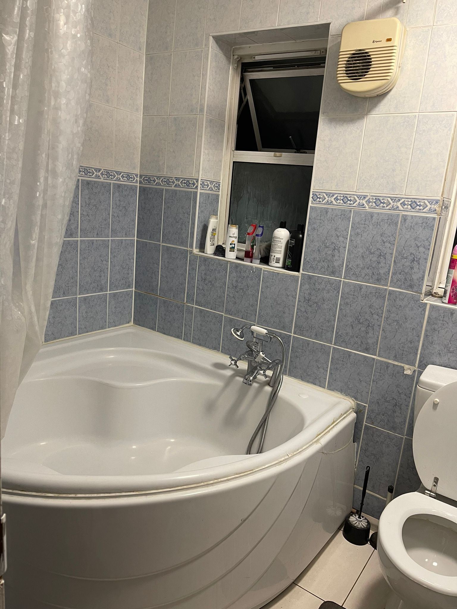 A bathroom with a bathtub, toilet, and a shelf with toiletries.