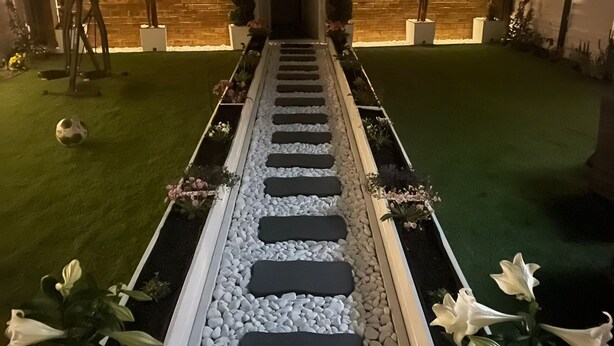 A pathway leading to a house with a brick facade, surrounded by a well-maintained garden with white flowers and a lawn. - Heathrow Garden Lodge [Free Parking • Netflix • Prime • Coffee • WiFi] (Hayes)