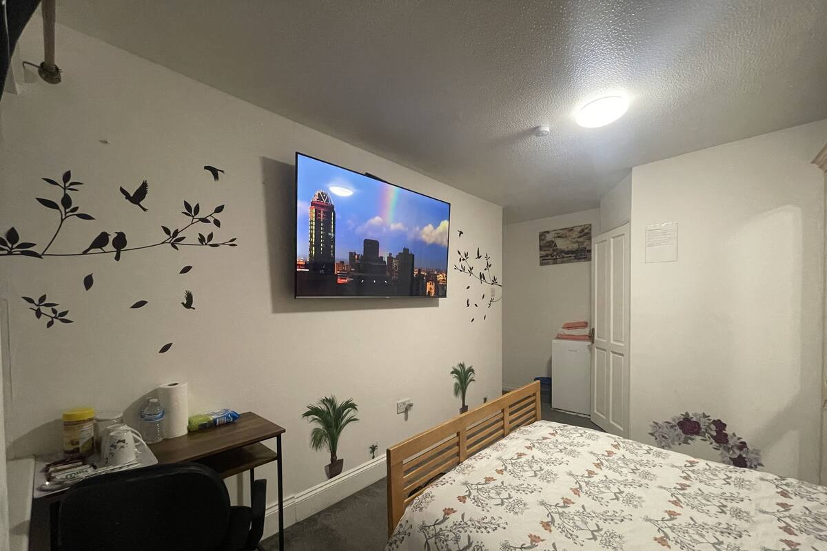 Een slaapkamer met een bed, een bureau met stoel, een televisie aan de muur en een deur.