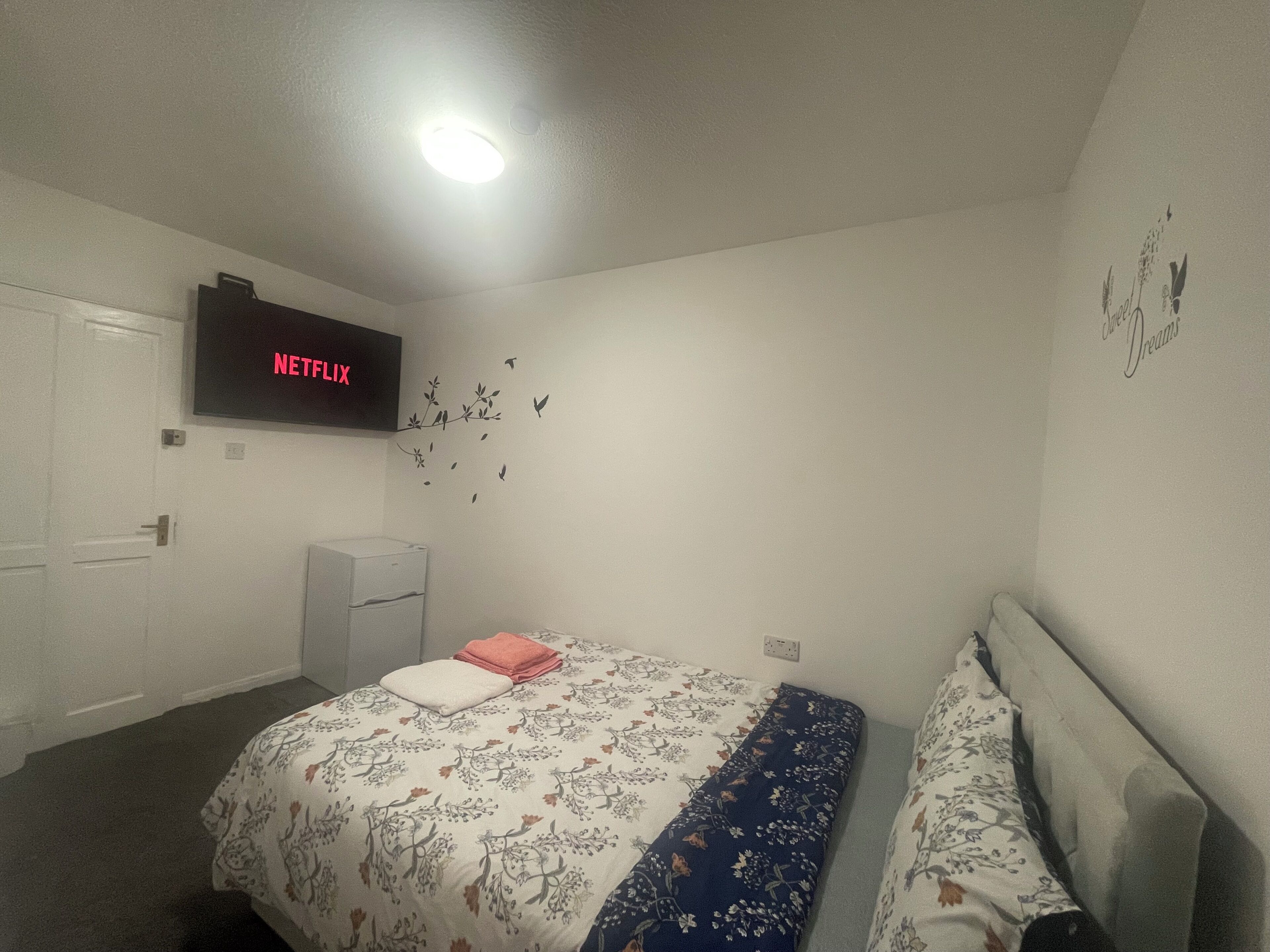 A bedroom with a bed, a TV mounted on the wall, a dresser, and a wall decal.