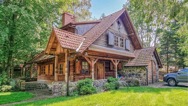 Eine Holzhütte mit Steinfundament, einem steilen Dach und einer Veranda mit Holzgeländern.